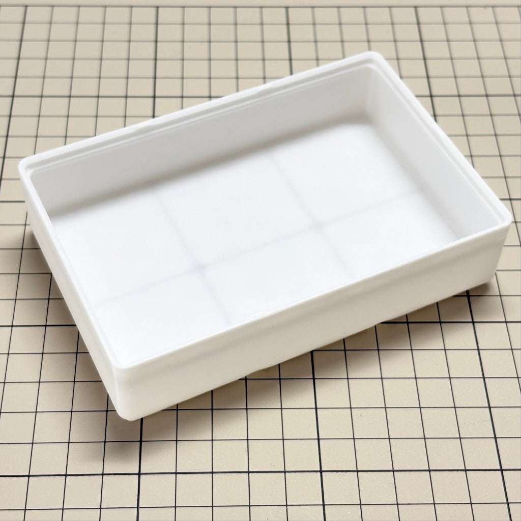 A white rectangular plastic tray with a gridfinity design inside, shown on a beige cutting mat with black grid lines.