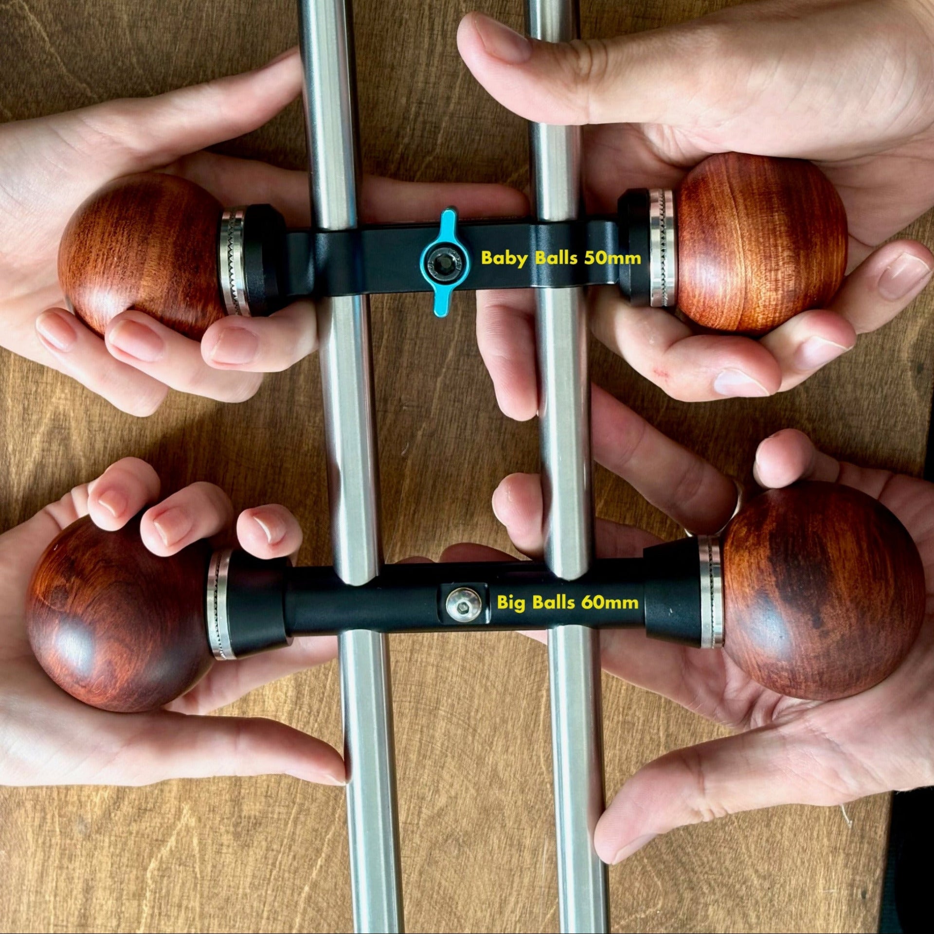 Two pairs of hands holding metal bars with wooden ball camera handles on a wooden surface.