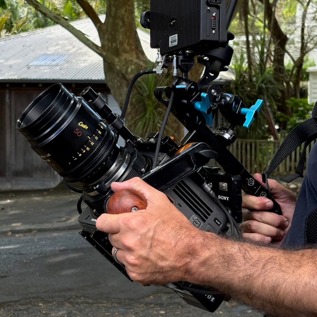 Person holding a wooden camera handle mounted to a Sony Burano camera with a 50mm Cooke S4 mini lens on it.