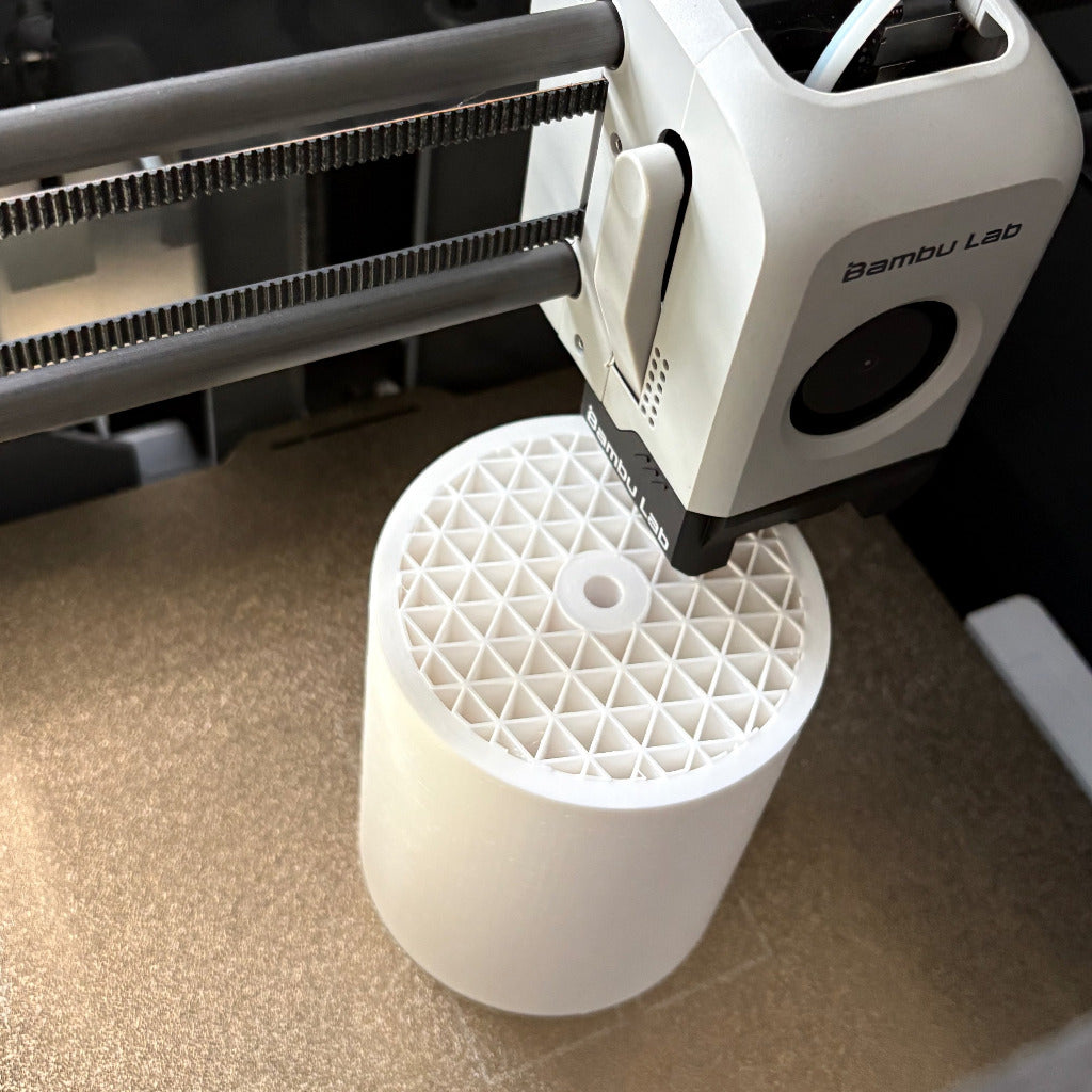 3D printer in action with a cylindrical white object being printed on a brown surface.
