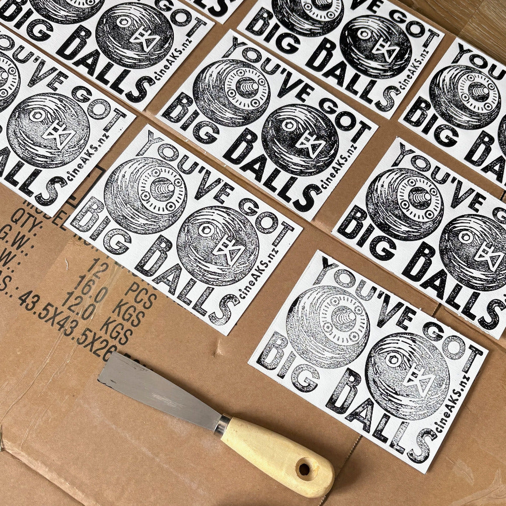 Multiple 'You've Got Big Balls' prints on a cardboard surface with a chisel.