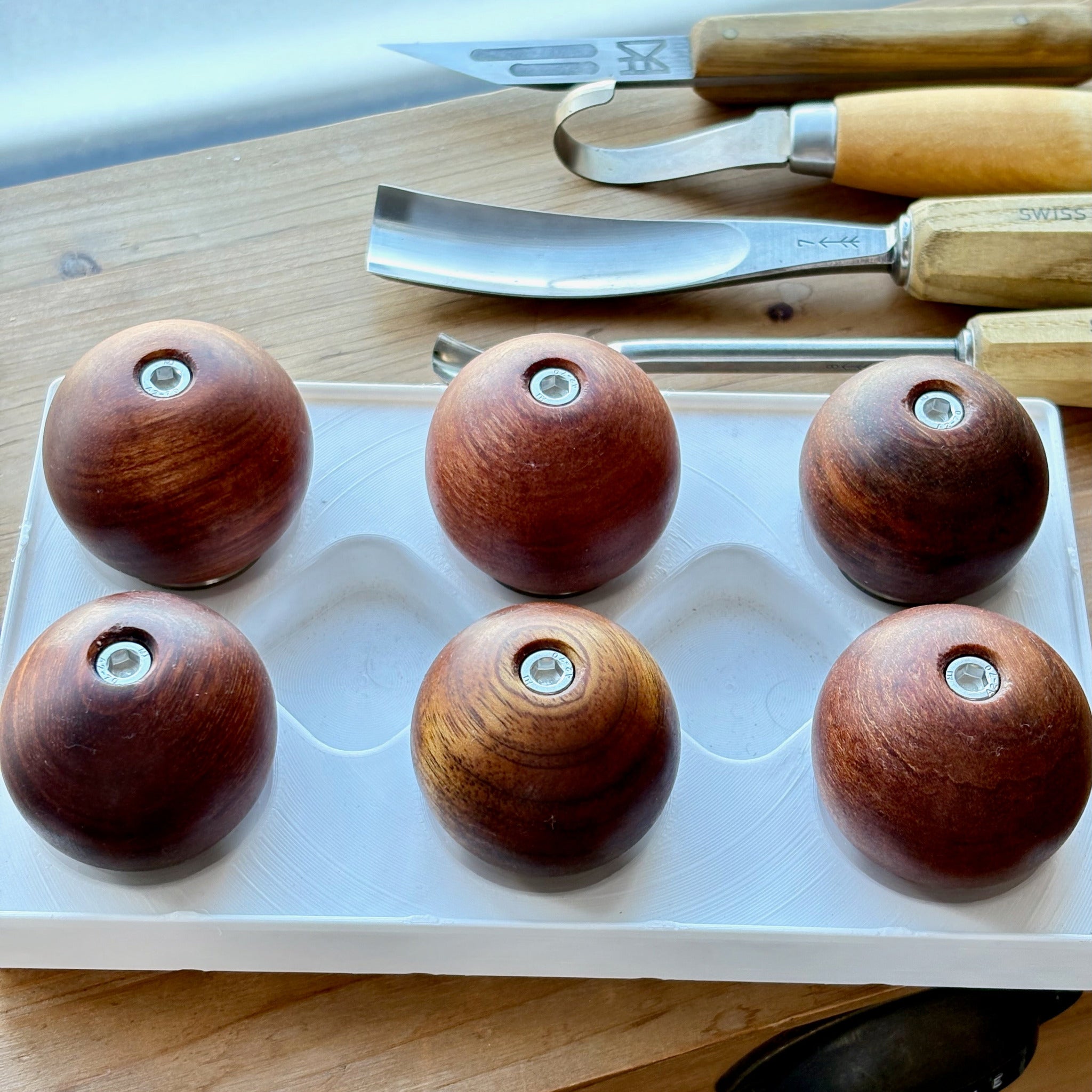Wooden ball camera handles on a white tray with carving tools in the background
