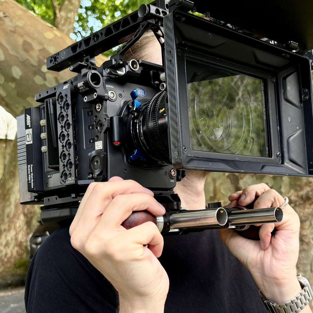 Person holding an Arri Alexa 35 Xtreme camera with Cooke S4 lens using wooden ball camera grips outside