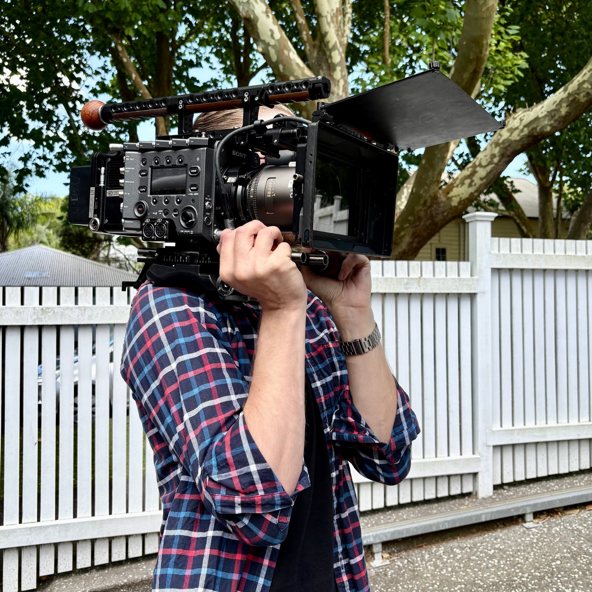Person holding a Sony Venice cinema camera with Atlas Mercury anamorphic lens outdoors with trees and a white fence in the background