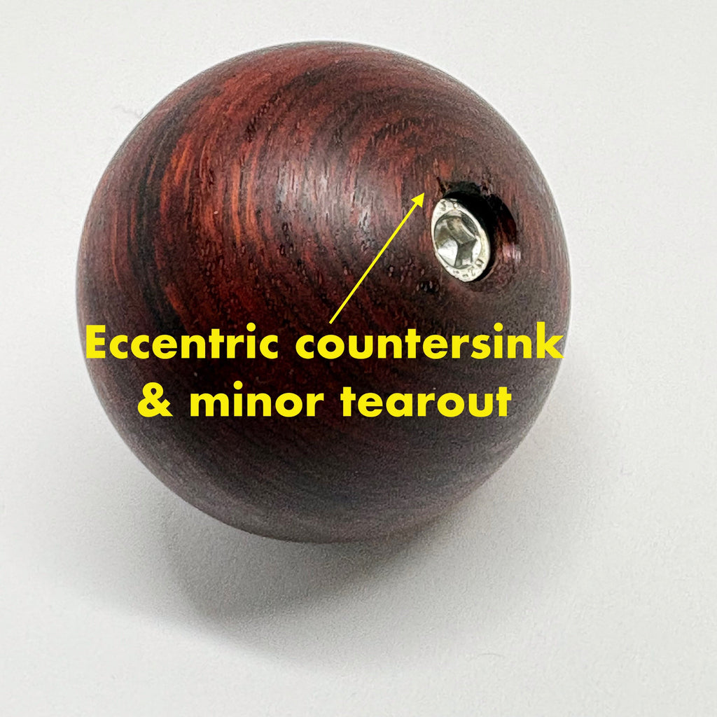 Wooden ball with a metal screw and text indicating 'Eccentric countersink & minor tearout' on a white background.