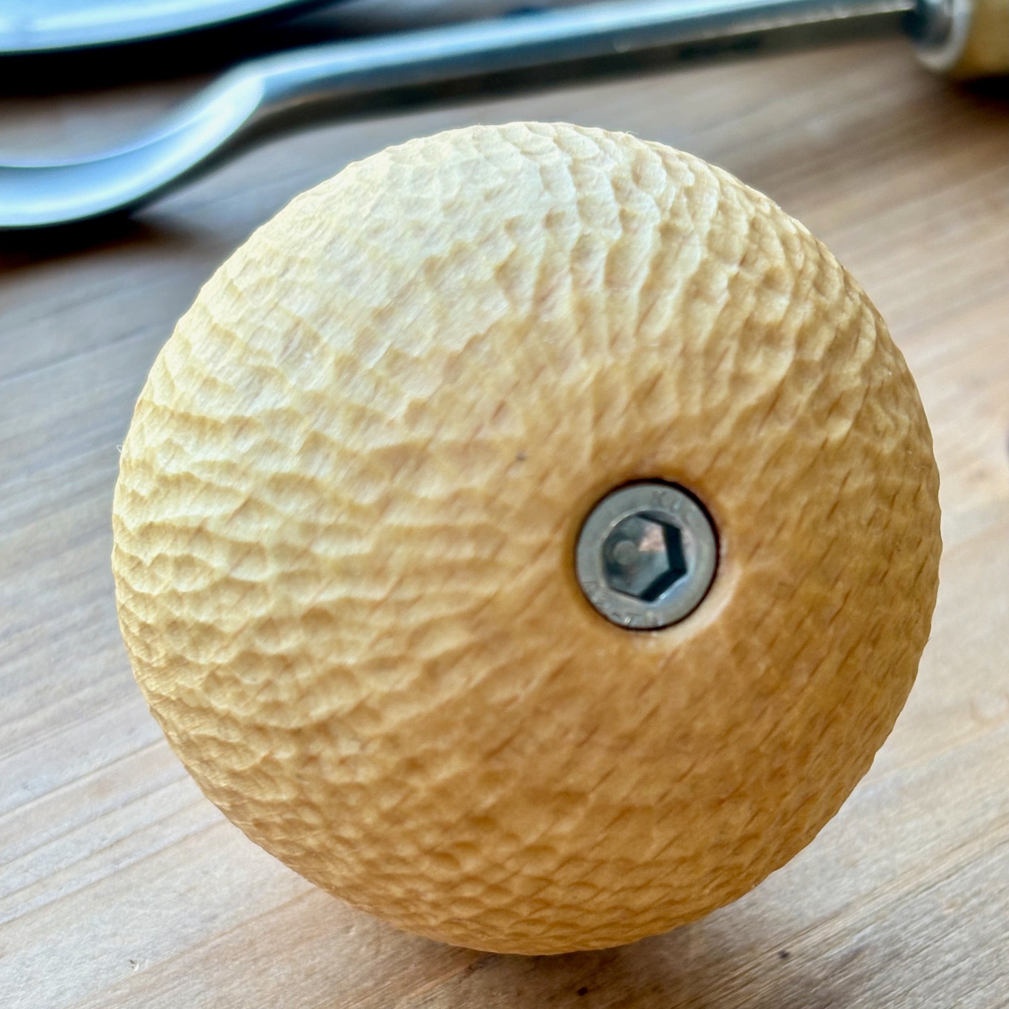 Beech wooden camera handle hand carved with a metal screw on a wooden surface