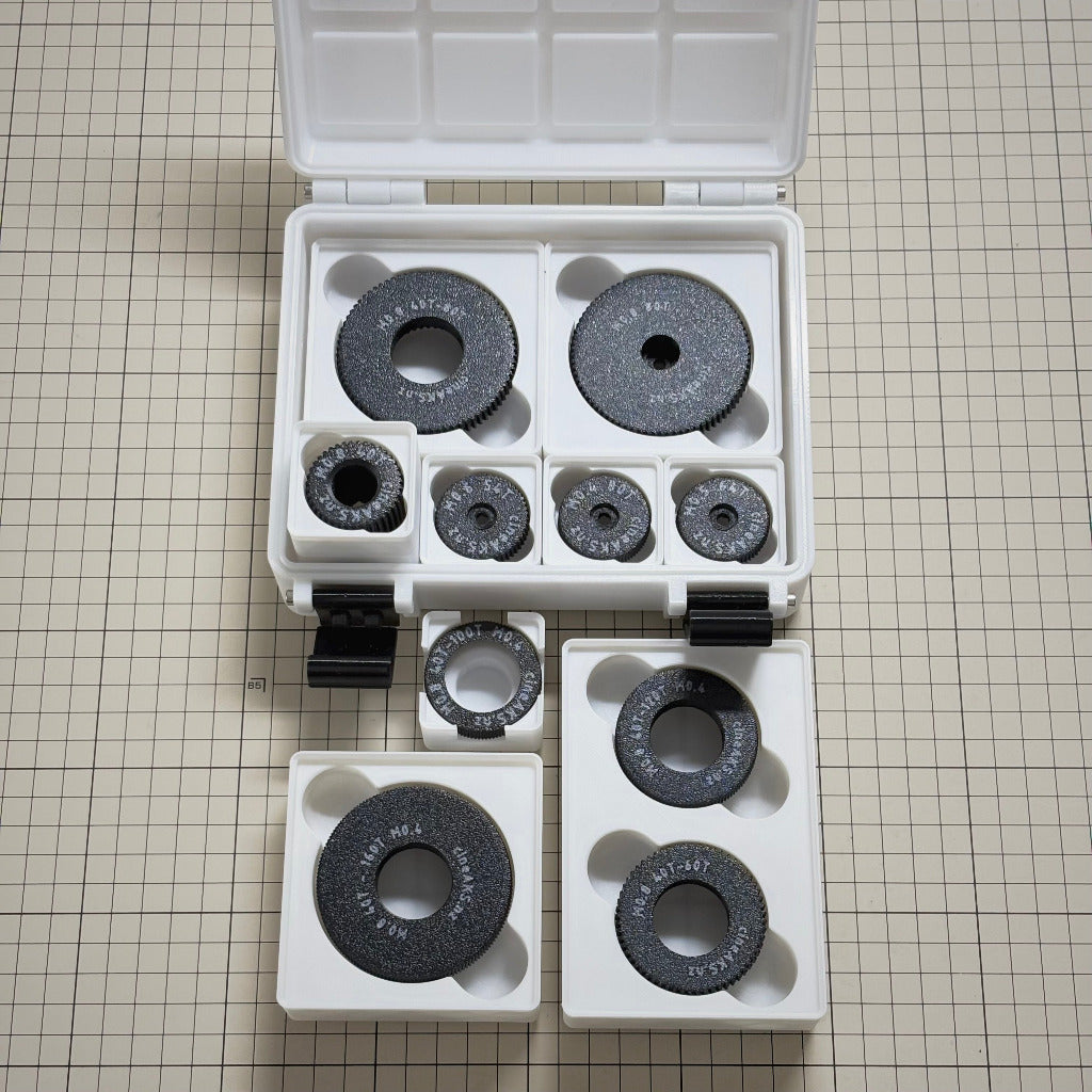 A cineAKS cforce Starter Kit with 10 direct-fit and push-on cinema lens gears, in a case with gridfinity modular storage bins. Photographed on a beige cutting mat.