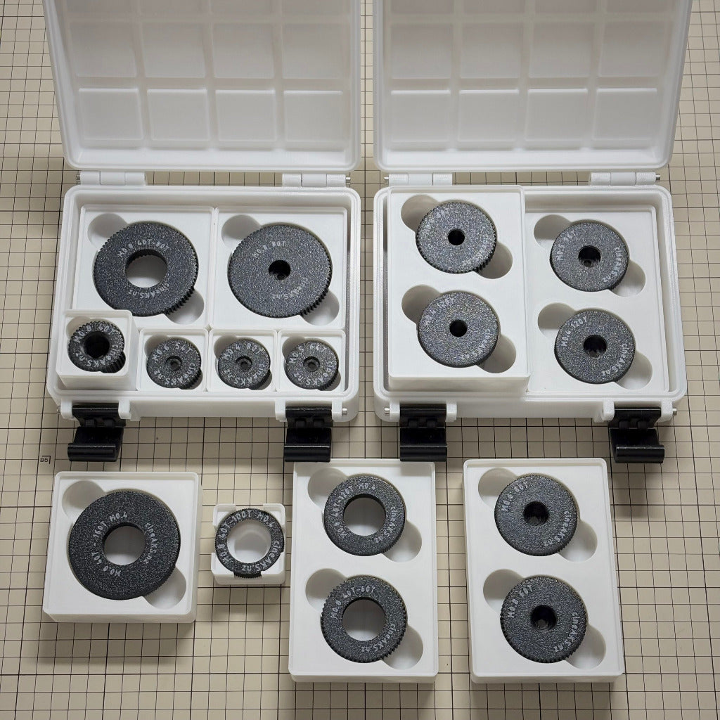 cineAKS cforce gear kits with M0.8, M0.6, M0.5 and M0.4 / 64p cinema lens gears stored in a 3x4x8U Gridfinity case on a beige grid surface.