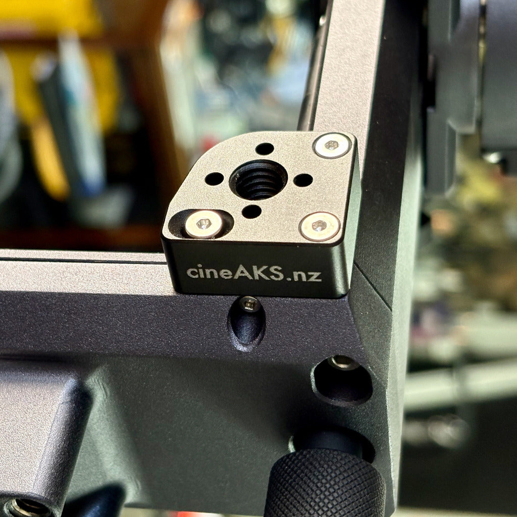 Close-up of a Cine Aks camera mounting bracket with the brand name 'cineAKS.nz' printed on its side, attached to a MotoCrane TitanLT camera gimbal.