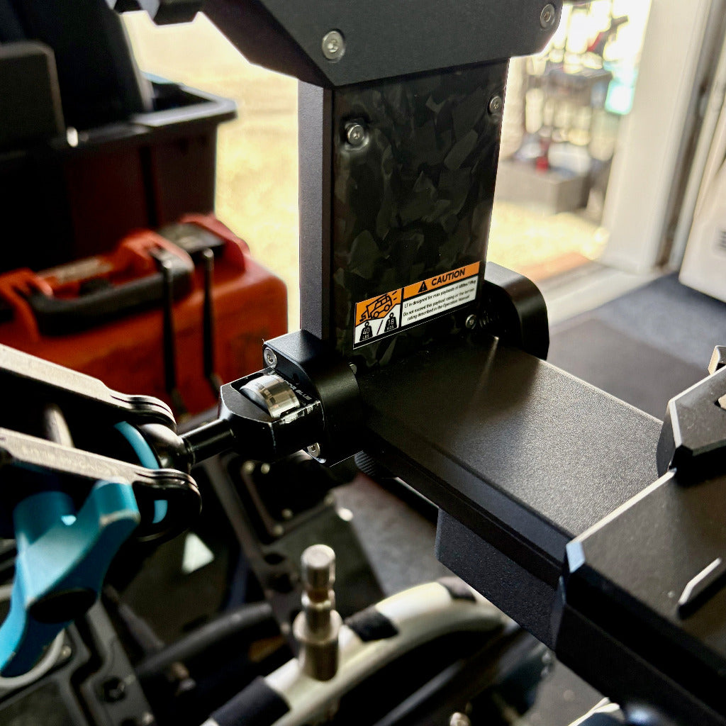Close-up of a black metal mounting bracket magic arm assembly on a TitanLT stabilised head  photographed in a workshop or garage setting with tools and a door visible in the background.